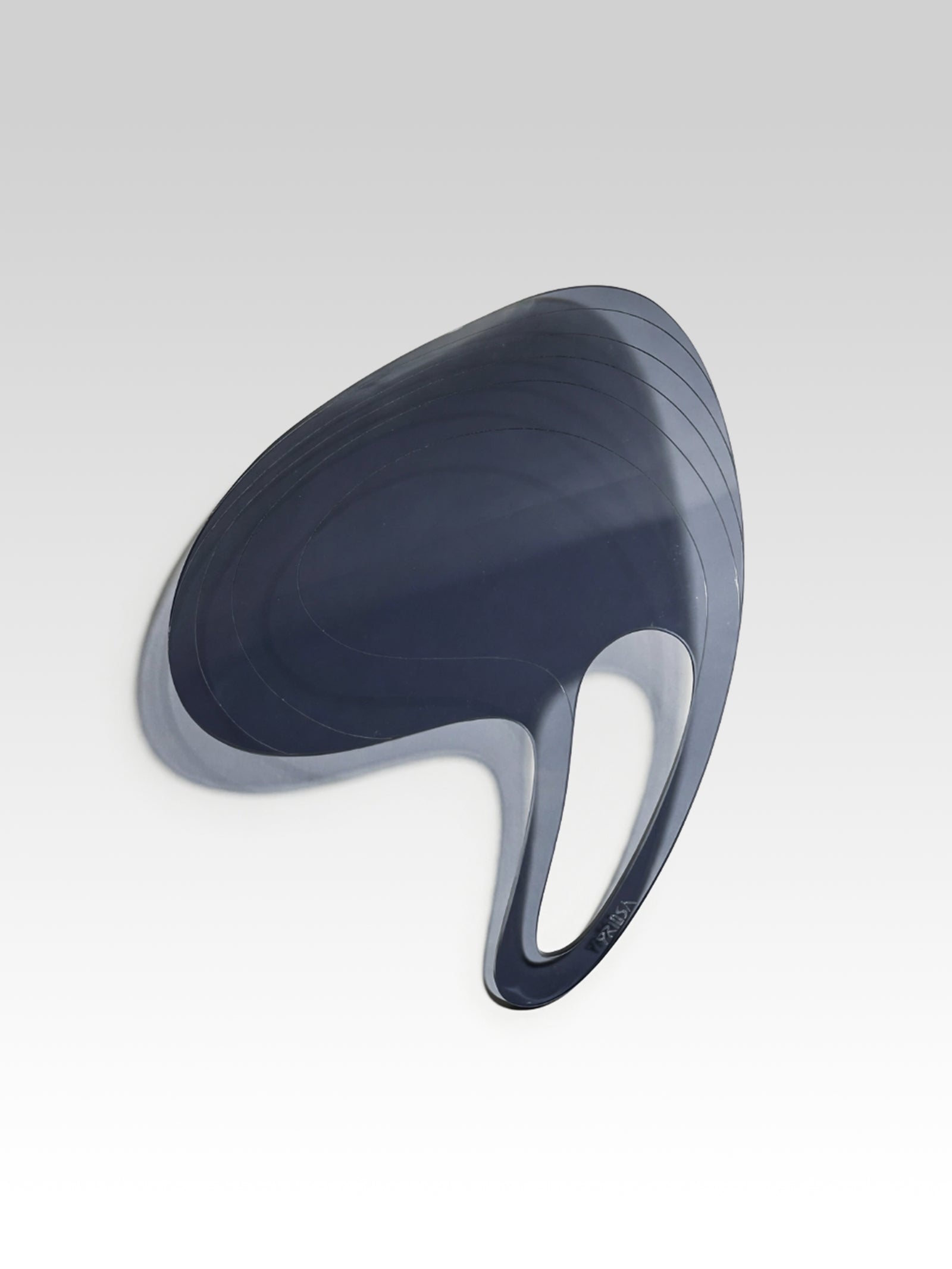 PRIOSA Prima clear acrylic design object photographed in high-contrast black and white, polished edges glowing against a pure black background, revealing the paisley silhouette, heat-bent bow profile, and PRIOSA logo engraving
