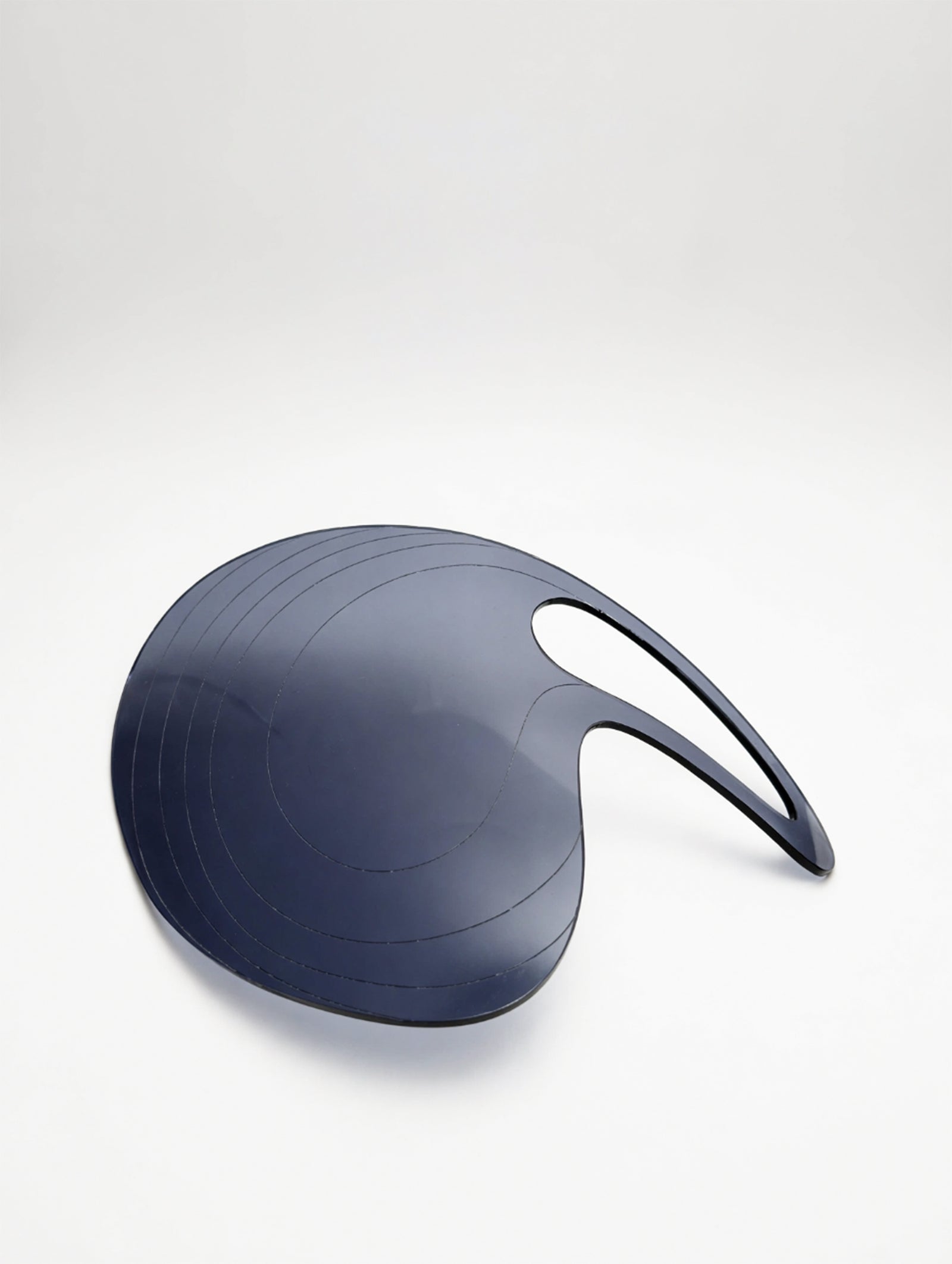 PRIOSA Prima — smoke grey translucent cast acrylic design object with concentric laser-etched topographic lines and ergonomic palm-grip opening, studio shot on dark background with warm ambient light
